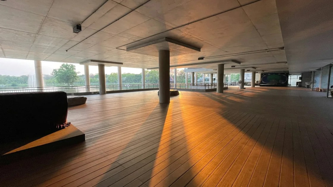 Sala diáfana de suelo de madera con columnas y luz cálida entrando de lado